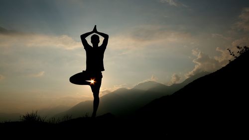 Silhouette man performing yoga against sky at dusk