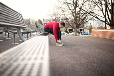 Sporty man wearing shoes while sitting on bench at park