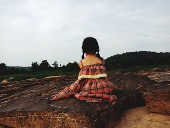 Woman sitting on land against sky