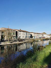 Buildings by river against clear blue sky