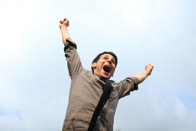 Low angle view of excited man with arms raised against sky