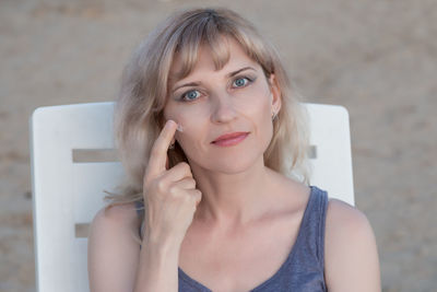 Close-up portrait of beautiful mature woman applying cream while sitting on bench in park