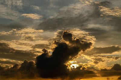 Low angle view of sunlight streaming through clouds during sunset