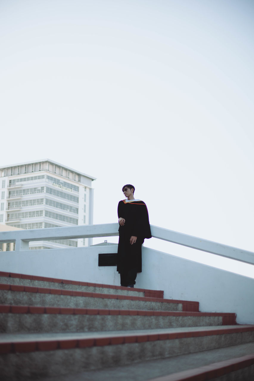 LOW ANGLE VIEW OF MAN STANDING AGAINST SKY IN CITY