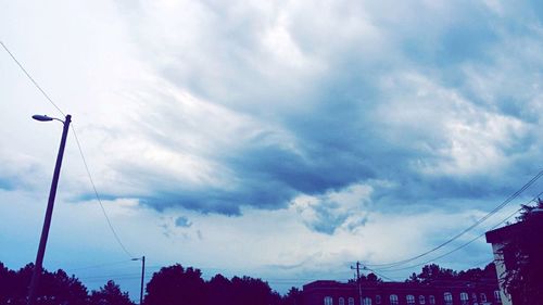 Low angle view of electricity pylon against cloudy sky