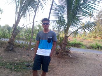 Full length of young man standing by palm trees