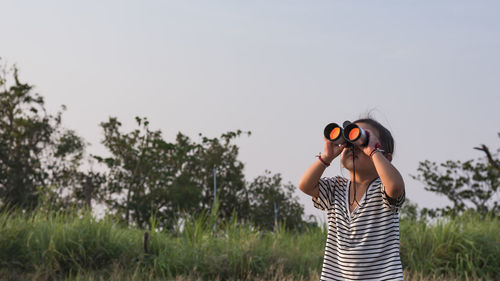 Rear view of woman photographing through binoculars against sky