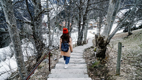 Rear view of woman moving down on steps in forest during winter