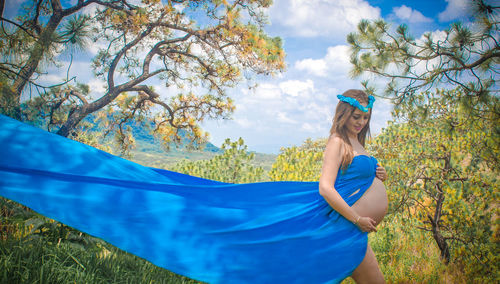 Pregnant woman wearing blue dress against trees
