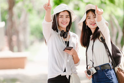 Portrait of smiling young woman holding smart phone standing outdoors