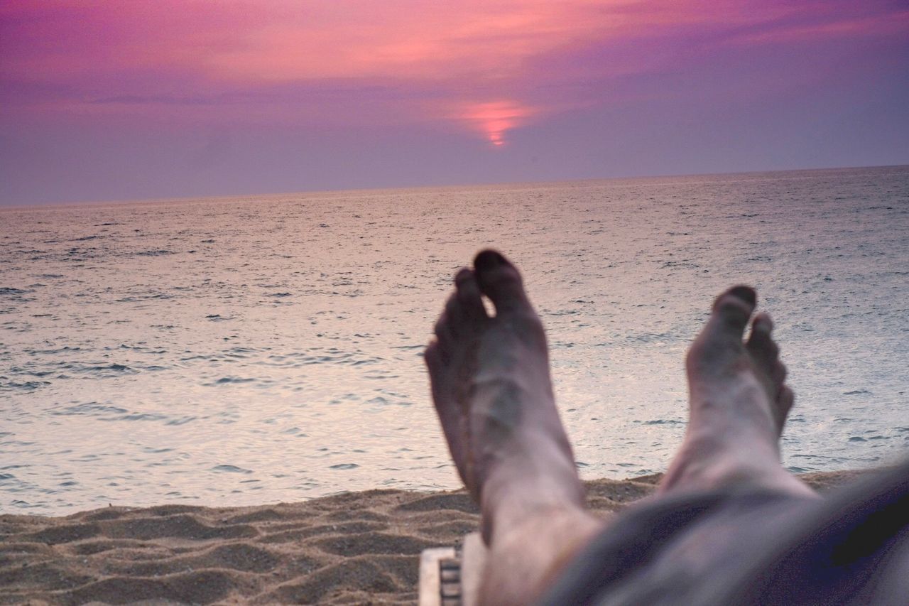 LOW SECTION OF MAN ON BEACH AGAINST SKY