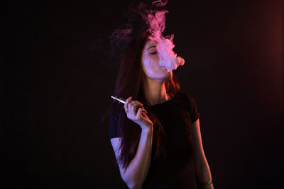 Young woman smoking cigarette against black background