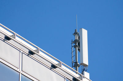 Low angle view of telephone pole against building against clear blue sky
