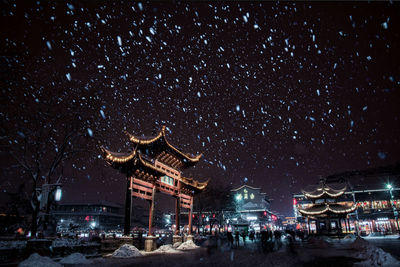 Illuminated buildings in city at night during snowfall