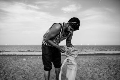 Man opening bag at beach against sky