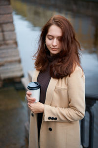 Woman holding disposable cup while standing by river in city