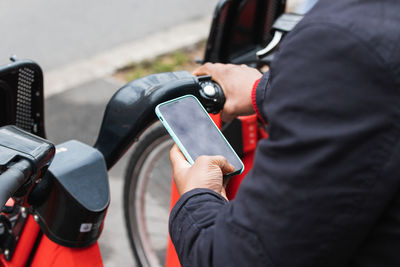 From above cropped unrecognizable masculine black male watching cellphone while using bike parking application in town