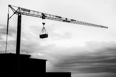 Low angle view of crane by building against sky