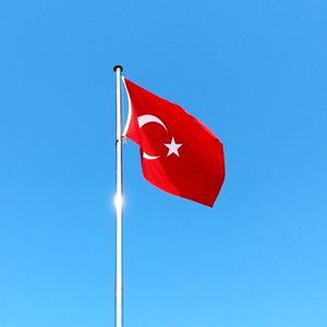 Low angle view of turkish flag waving against clear blue sky