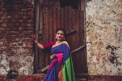 Portrait of young woman standing against wall