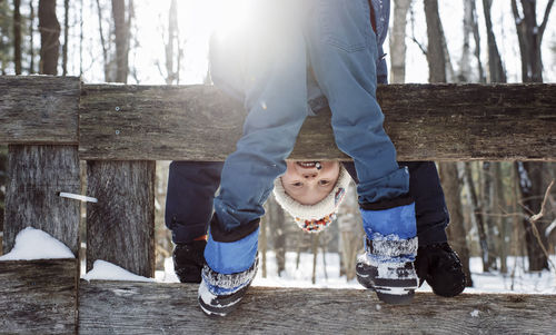 Portrait of happy boy bending while standing on fence during winter