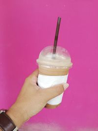 Cropped image of hand holding drink against pink wall