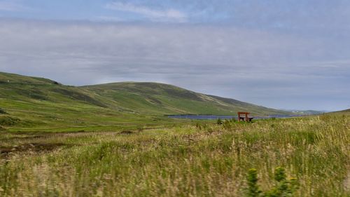 Scenic view of land against sky wirh red bench at shetlands