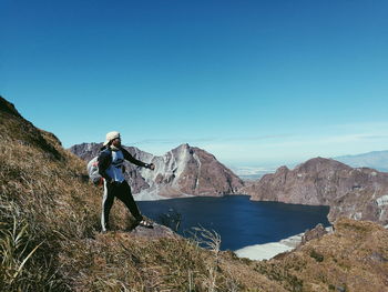 Full length of man on rocks against clear blue sky