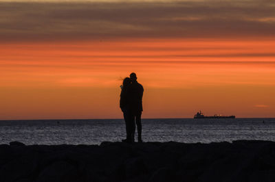 Silhouette man standing on beach against orange sky