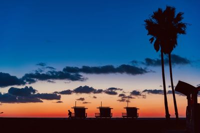 Silhouette palm trees by building against sky during sunset