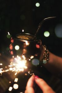 Tilt shift image of cropped woman holding burning sparkler with drink