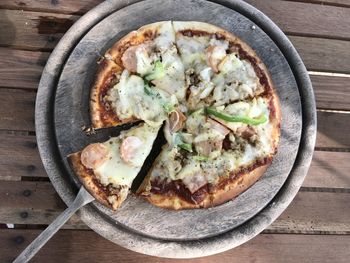 Sausages and bell pepper pizza served on round wood plate with wood spoon, put on wood table