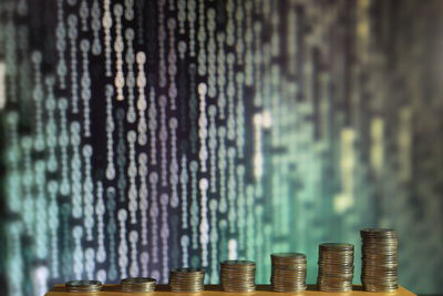 Stacked coins against binary code on screen