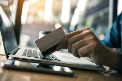 Cropped image of man holding credit card on laptop