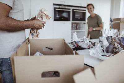 Midsection of male unpacking cardboard box while smiling female standing in new house