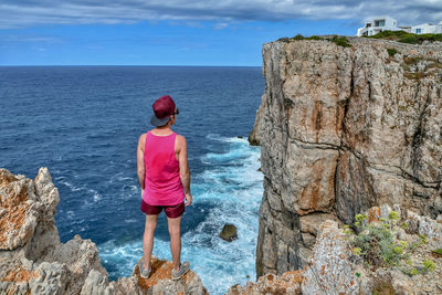 Rear view of man standing on rock looking at sea against sky