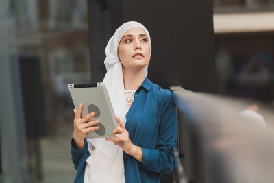 Young woman holding digital tablet standing outdoors