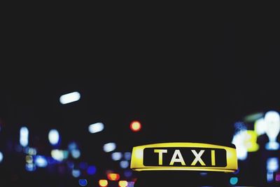 Close-up of taxi sign against illuminated lights at night