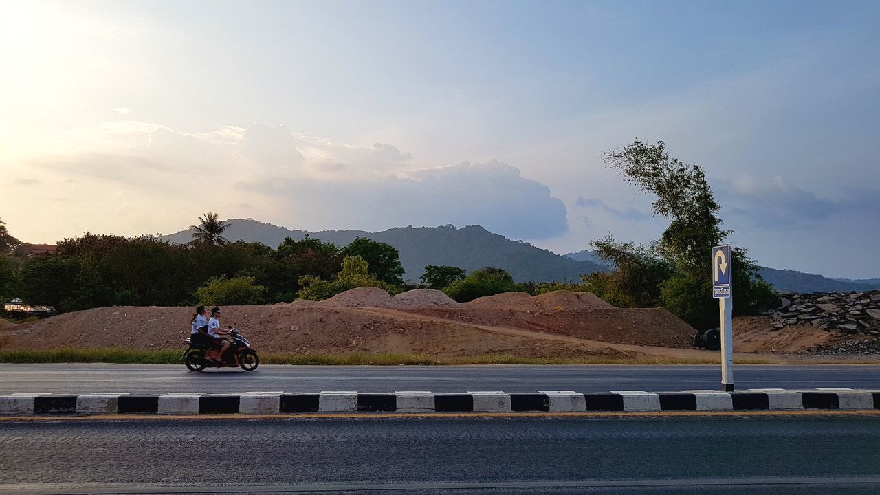 MAN RIDING BICYCLE ON ROAD AGAINST MOUNTAIN