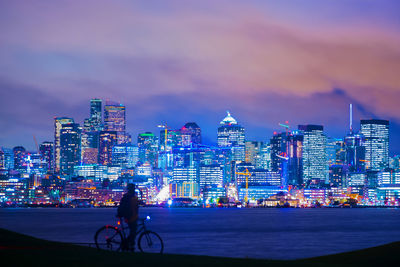 Man and bicycle against illuminated buildings in city at dusk