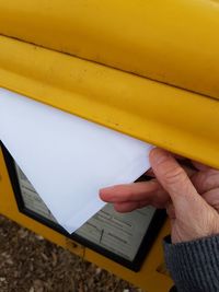 Cropped hand of person holding blank envelope by yellow mailbox