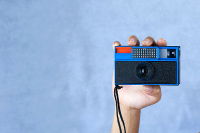 Cropped hand holding camera against wall