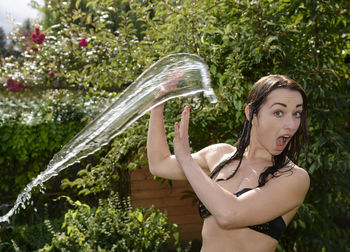 Water splashing on surprised woman in yard against trees