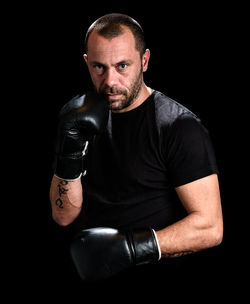 Portrait of mid adult man wearing boxing gloves against black background