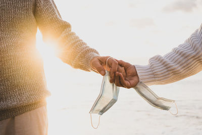 Cropped hands of couple with mask against sea