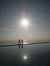 Silhouette people standing on beach against sky during sunset