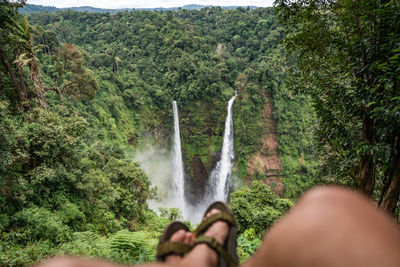Low section of man sitting against waterfall