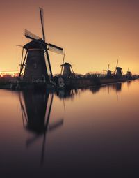 Traditional windmill by river against sky during sunset