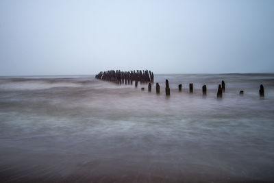 Wooden posts in sea against clear sky