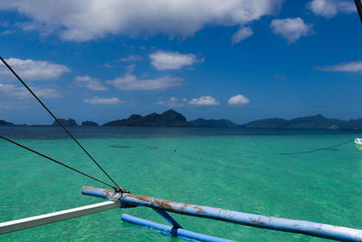 Cropped image of outrigger boat in turquoise sea against sky
